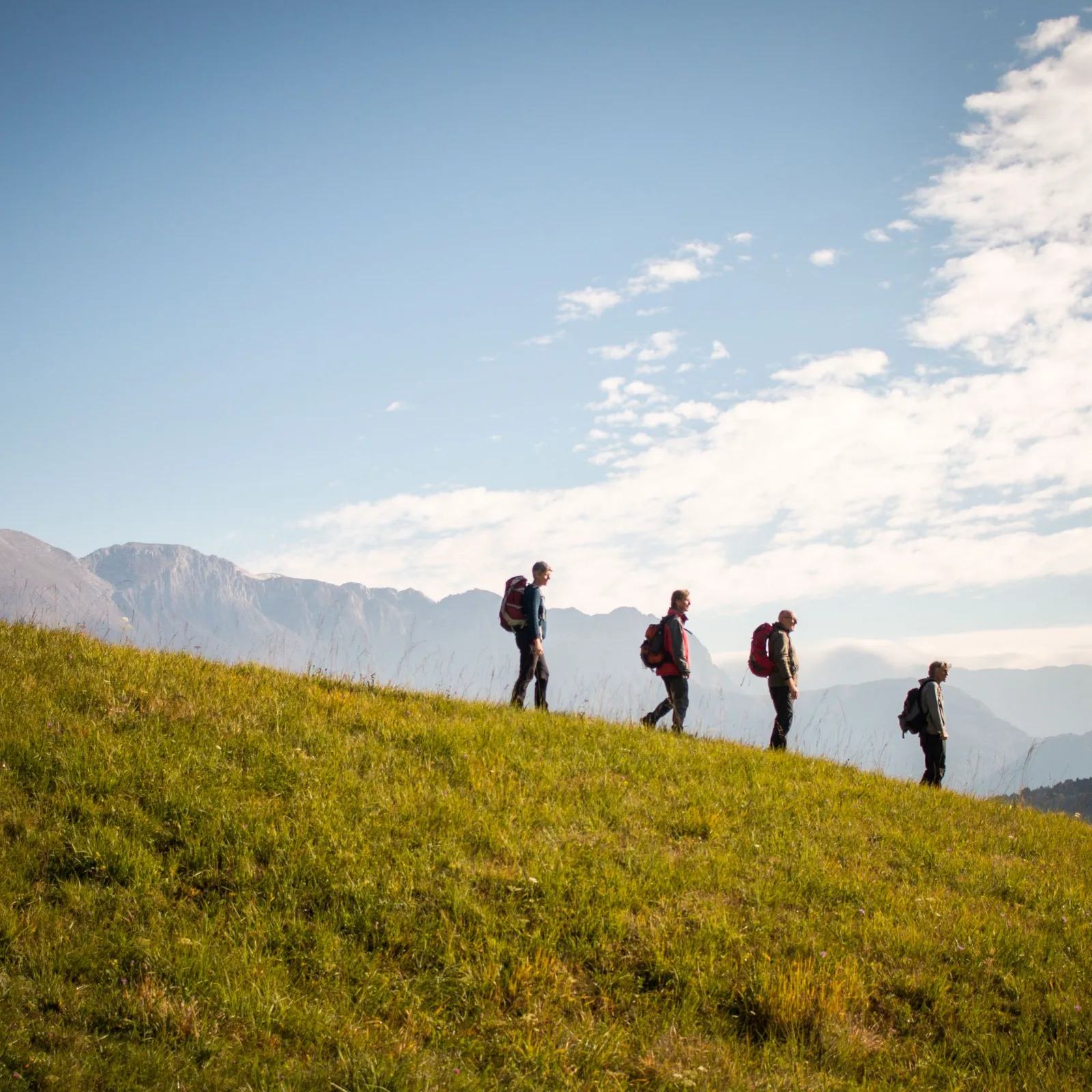 People hiking down a grassy hillside.